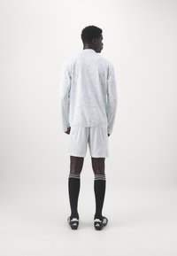 Hvid langærmet sports skjorte med et geometrisk mønster, parret med hvide shorts og sorte knæhøje sokker med striber, båret med fodboldstøvler.