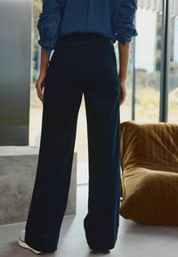 Pantaloni largi de marină, confecționați dintr-un material moale, cu talie înaltă și textură netedă. Asortați cu o cămașă din denim albastru și adidași albi.