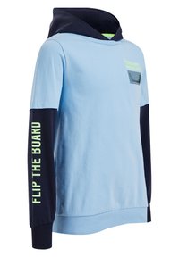 Ljusblå hoodie med marinblå huva och ärmar, neongrön text "FLIP THE BOARD" på vänster ärm och liten grafik på bröstet.