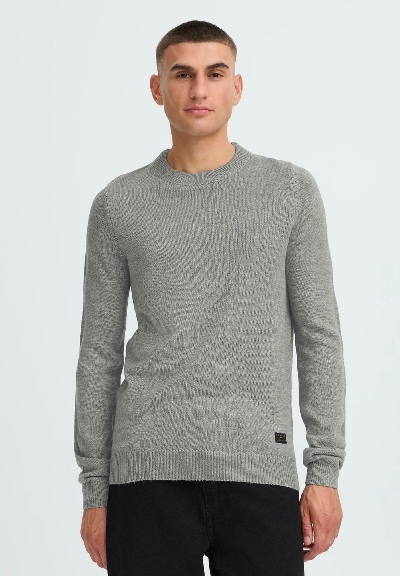 Light gray knit sweater with a round neckline, long sleeves, ribbed cuffs, and hem. Features subtle texture and a small logo at the bottom.