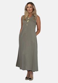 Długa, bezrękawnikowa sukienka w oliwkowym kolorze, z prostym krojem, z wyszywanymi guzikami z przodu i bocznymi kieszeniami. Noszona z butami na otwartym palcu.