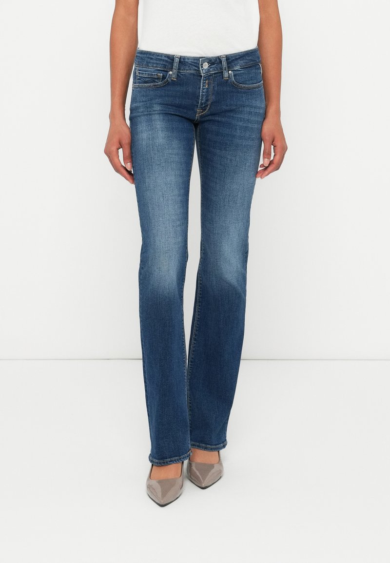 Jeans en denim évasés de couleur bleu moyen avec un léger dégradé. Comprend cinq poches, des finitions argentées et une fermeture à bouton classique. Texture douce.