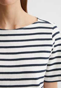 Gestreiftes Kurzarmoberteil aus weißem und navyfarbenem Stoff, mit einem weiten Ausschnitt und einer sanften Textur sowie gleichmäßig verteilten horizontalen Streifen.