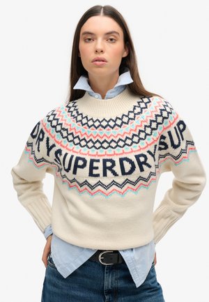 Suéter de punto crema con patrones geométricos en azul marino, coral y azul claro. Presenta la palabra "SUPERDRY" de manera destacada en el frente.