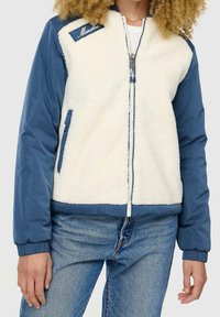 Veste bomber légère avec un corps crémeux duveteux et des manches bleu marine, fermeture éclair et poches avant avec des poignets côtelés.