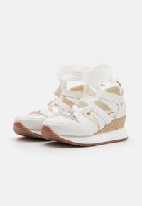 White wedge sneakers with a textured mesh upper, sleek design, contrasting rubber sole, and decorative ribbon straps across the front.