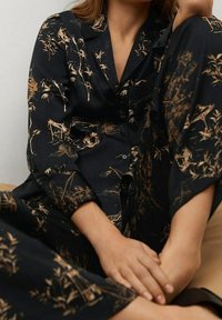 Conjunto de pijama negro con patrones florales decorativos en beige y escenas, que incluye una camisa con cuello y pantalones sueltos, fabricado con tela suave.