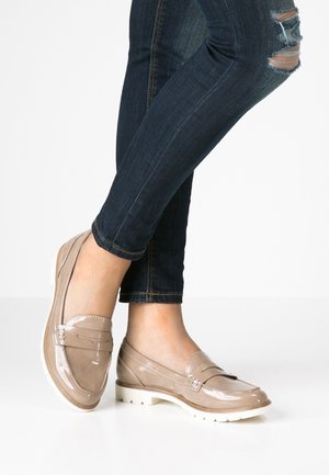 Beige patenterede læder loafers med broderet design og dekorativ hardware, med hvid gummisål og rund tå, båret med mørke jeans.