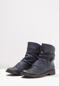 Botas de cuero hasta el tobillo en azul oscuro, de diseño holgado con puntera redonda, suela texturizada y pequeño hardware decorativo en el costado.