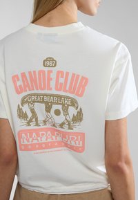 Witte katoenen t-shirt met een grafische print van kanoërs, bomen en de tekst "CANOE CLUB GREAT BEAR LAKE" in roze en bruin.