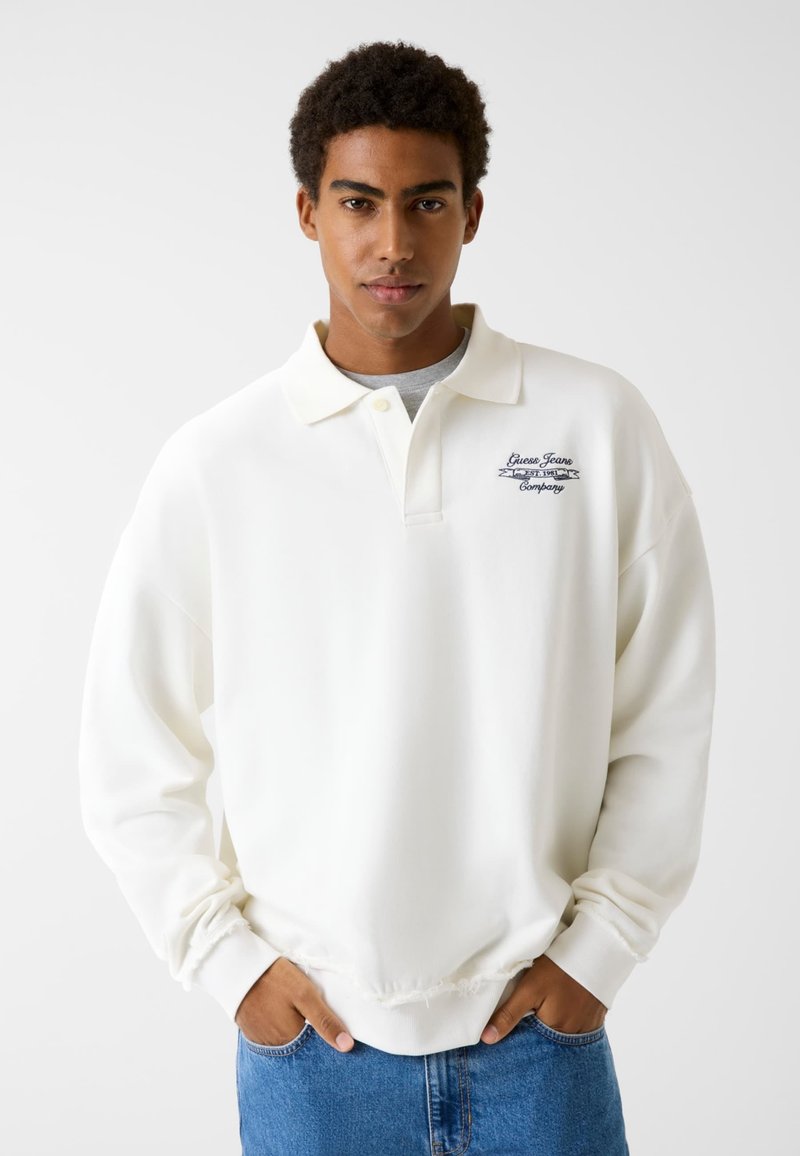 White polo sweatshirt with a relaxed fit, ribbed cuffs, and a small navy logo on the chest. Soft fabric with a smooth texture.