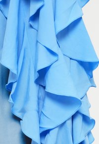 Robe bleu clair avec des volants superposés, une texture de tissu lisse et une coupe fluide. Les volants ont un bord ondulé pour un détail supplémentaire.