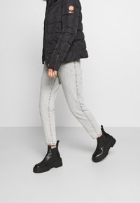 Black puffer jacket with zipper, gray jeans, and black leather ankle boots with a chunky sole. The boots feature a pull tab and smooth finish.