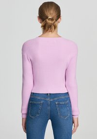 Jasnoróżowy sweter prążkowany z długimi rękawami i skróconym krojem, w komplecie z niebieskimi dżinsami z tylnymi kieszeniami.