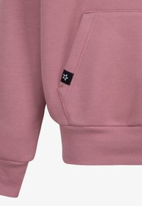 Rózsaszín pulóver kenguruzsebével, bordázott mandzsettákkal, valamint az oldalán fekete címkével, amelyen fehér csillag látható. Sima textúra.