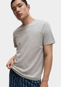 Šedé bavlněné tričko s krátkým rukávem, kulatým výstřihem a jemným předním švem, nošené s pruhovanými pyžamovými kalhotami.