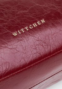 Rode leren handtas met een gestructureerde afwerking, voorzien van een gouden "WITTCHEN" logo. Zachte randen en subtiele stikseldetails zichtbaar.
