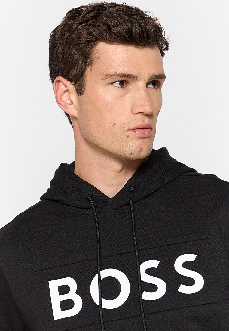 Hoodie noir en tissu doux, avec un grand imprimé blanc "BOSS" sur le devant. Comprend une capuche avec cordons et des poignets côtelés.