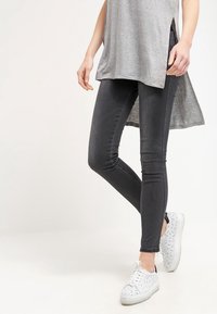 Svarta skinny jeans i denim med en len yta, tillsammans med en lång grå tunika och vita mönstrade sneakers.