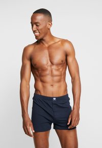 Marinelogekatoenen boxershorts met een knoopsluiting, elastische tailleband en logoaccent. Gladde textuur en aansluitend design. Korte lengte.