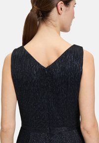 Czarna sukienka o teksturowej powierzchni, bez rękawów, z dekoltem w kształcie litery V z tyłu. Posiada dyskretny zamek. Materiał ma subtelne, błyszczące nitki.