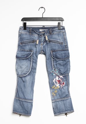Pantalones cargo de mezclilla con un lavado azul, múltiples bolsillos grandes y bordados florales en la pierna izquierda. Presenta cremalleras y cuentas decorativas.