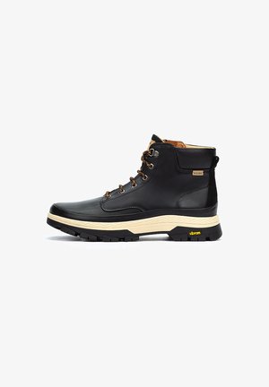 Bota de senderismo de cuero negro con detalles en marrón, collar acolchado, diseño con cordones, suela texturizada y marca Vibram en el borde de la suela.