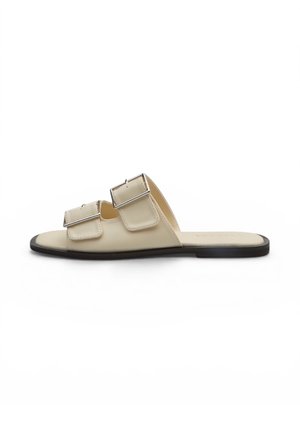Sandalo beige open-toe con due fibbie argentate regolabili e suola piatta nera, mostrato di profilo su sfondo bianco.