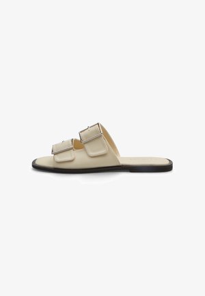 Sandalo beige open-toe con due fibbie argentate regolabili e suola piatta nera, mostrato di profilo su sfondo bianco.