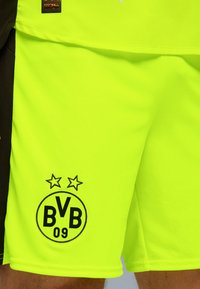 Shorts da calcio giallo neon con una texture traspirante, dotati di un logo nero con "BVB 09" e due stelle. Pannello laterale in nero a contrasto.