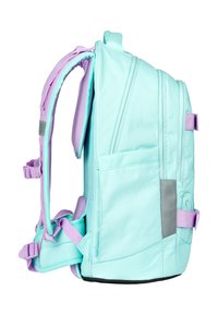 Zaino verde menta con dettagli in lavanda, spallacci imbottiti, tasche laterali, una toppa grigia e un design strutturato. Comparti con cerniera frontali visibili.