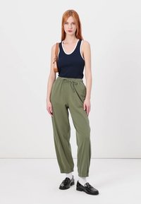 Mørkeblå tanktop med hvid halsudskæring, løstsiddende grønne joggers med elastisk talje, parret med sorte loafers og hvide sokker.