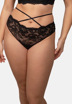 Black lace high-waist panties with floral pattern and crisscross straps worn by a person against a white background.