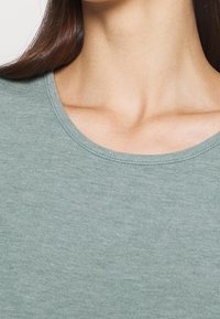 Sovitehty t-paita pyöreällä kauluksella hillityssä vihreässä värissä, valmistettu pehmeästä puuvillasekoitteesta, jossa on sileä поверхность ja vähäiset ompeluyksityiskohdat.