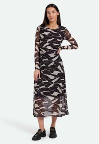 Langärmliges Kleid aus transparentem schwarzem Stoff mit geometrischen beigen und grauen Mustern. Verfügt über eine geraffte Taille und eine fließende Silhouette.