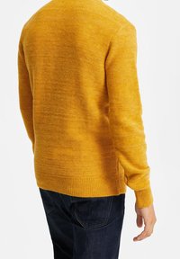 Stickad tröja i klar gul färg, med strukturerad yta, rund halsringning samt ribbade muddar och fåll; bärs med mörkblå jeans.