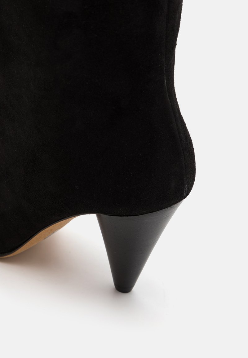 Black suede ankle boot with a tapered heel, featuring a smooth texture and minimalist design. The heel is matte black with a subtle curve.
