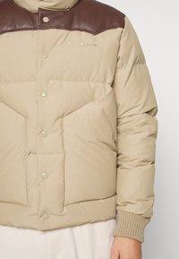 Veste matelassée beige avec empiècement en cuir marron, boutons-pression, deux poches avant, poignets côtelés et logo "Schott" sur la poitrine.