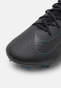 Czarne korki piłkarskie z teksturowanej syntetycznej cholewki, z czarnymi sznurówkami i subtelnym zielonym logo Nike. Zawierają niebieskie korki na podeszwie dla lepszej przyczepności.