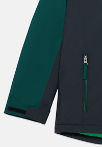 Casaco resistente à água com um corpo cinza escuro e mangas verdes, apresenta um bolso com fecho éclair, fecho éclair em contraste e fecho de velcro nos punhos.