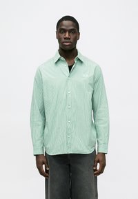 Cămașă cu dungi verzi, cu nasturi, cu croială lejeră, mâneci lungi, guler deschis și un logo subtil pe piept.