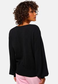 Pull en maille noir à coupe décontractée, avec épaules tombantes, manches longues et ourlet côtelé. Texture lisse avec des détails minimaux.