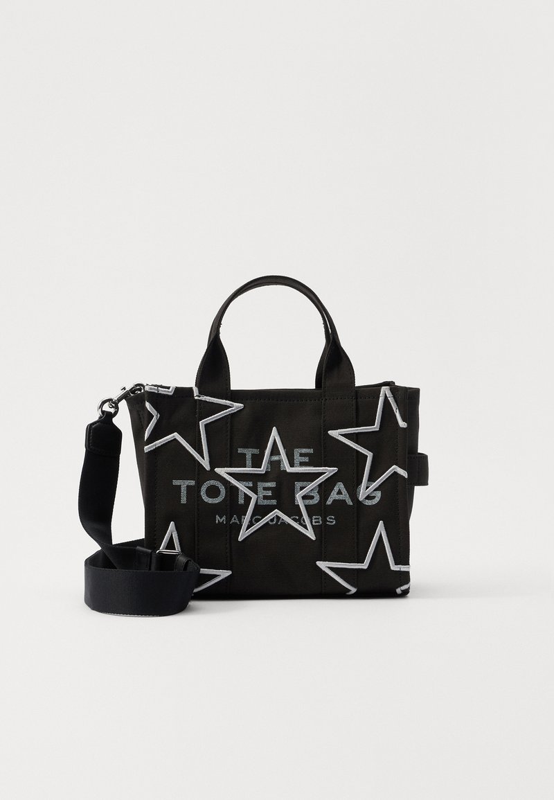 Black tote bag with white star outlines, short handles, and a detachable wide shoulder strap, showing printed text on front panel.