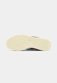 Shoe sole with a textured, herringbone pattern. Color scheme includes cream and teal, with a logo printed in a rectangular box.