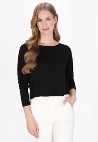 Schwarz cropped Langarmshirt mit weitem Ausschnitt, kombiniert mit weißen Hosen. Besitzt eine glatte Textur und einen lockeren Schnitt.