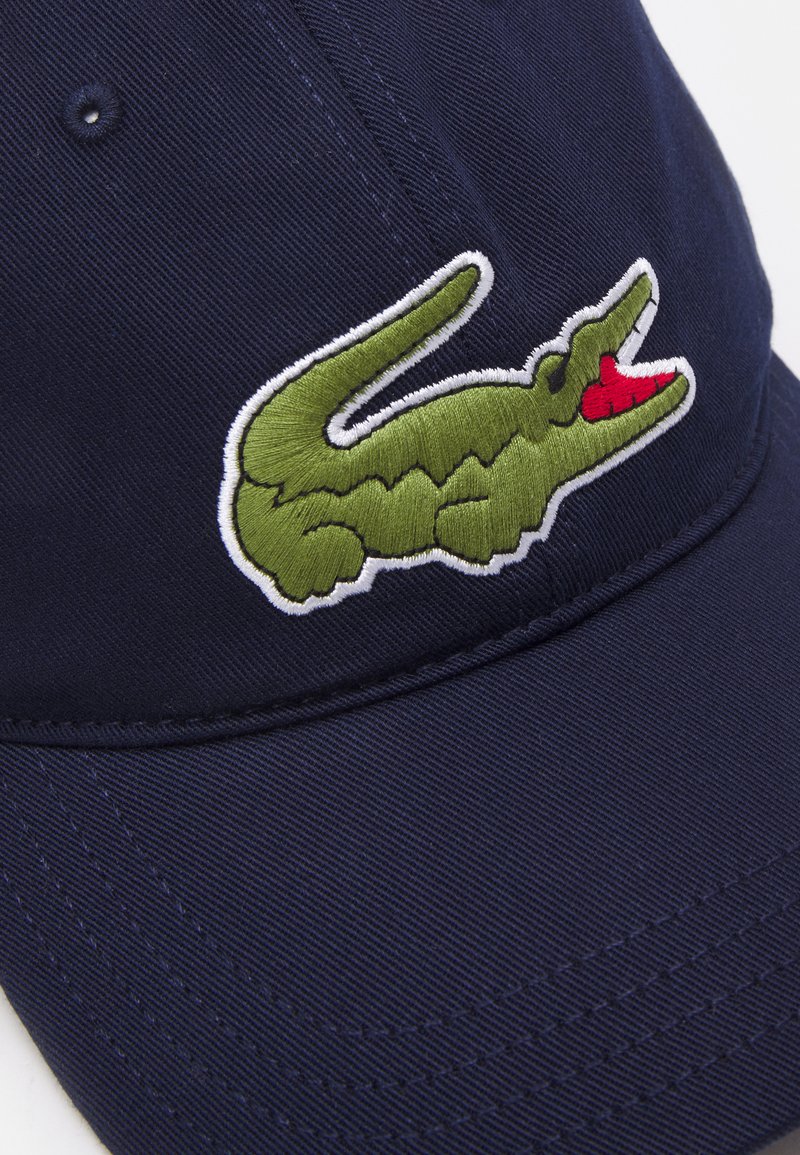 Cappello blu navy con logo di coccodrillo ricamato in verde e dettagli rossi sul davanti. Realizzato in un tessuto durevole e testurizzato.