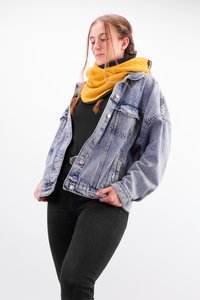 Denim jacket with light blue wash, relaxed fit, and silver buttons, paired with a chunky yellow knitted scarf and black top.