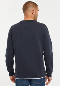 Marineblauwe sweatshirt met lange mouwen, een ronde hals, ribgebreide manchetten en een kleine horizontale naaddetail aan de achterkant. Zachte stoftextuur.