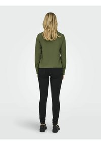 Dark green long-sleeve top, fitted silhouette, paired with black leggings. Smooth fabric, no visible patterns, minimalistic design.