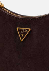 Borsa a mano in suede marrone con una placca logo triangolare dorata. Presenta una cerniera dorata lungo il bordo superiore e una texture morbida.